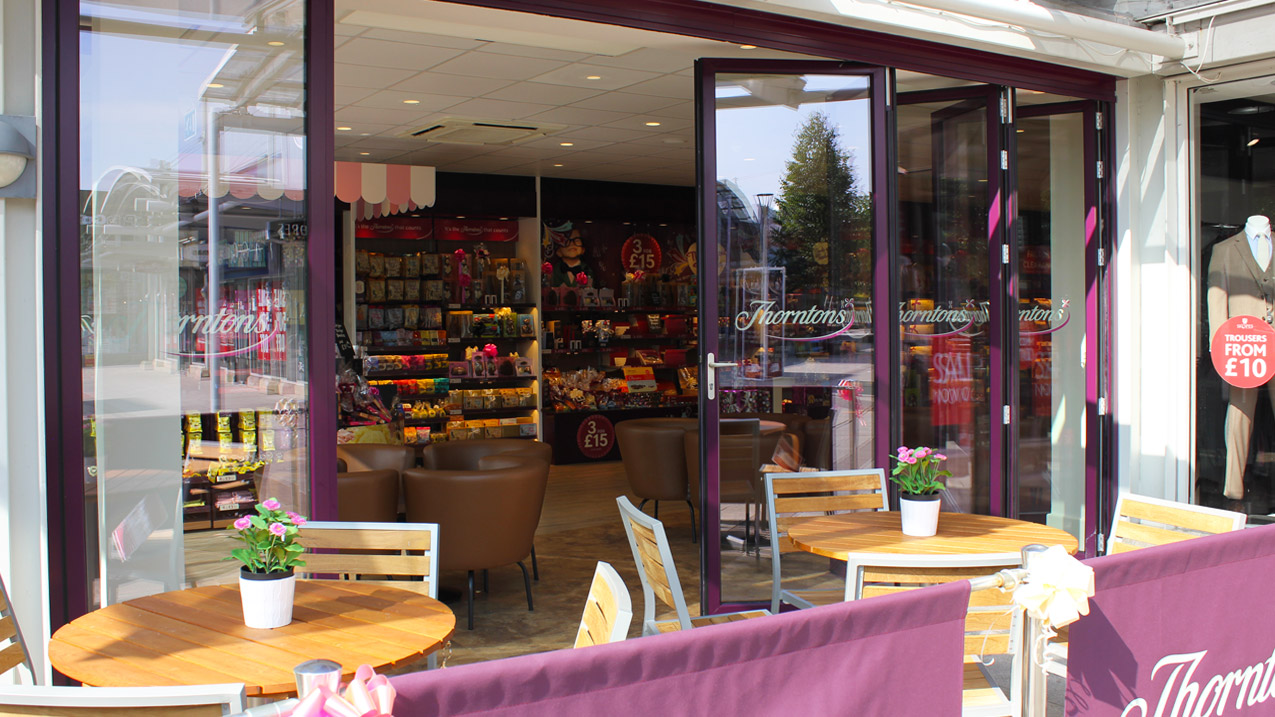 Photo of Thorntons Cafe (Castleford) with magenta powder coated aluminium bifold doors installed to two shop sides to create an indoor/outdoor dining terrace
